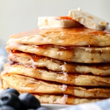 a stack of vegan protein pancakes topped with maple syrup and banana slices.