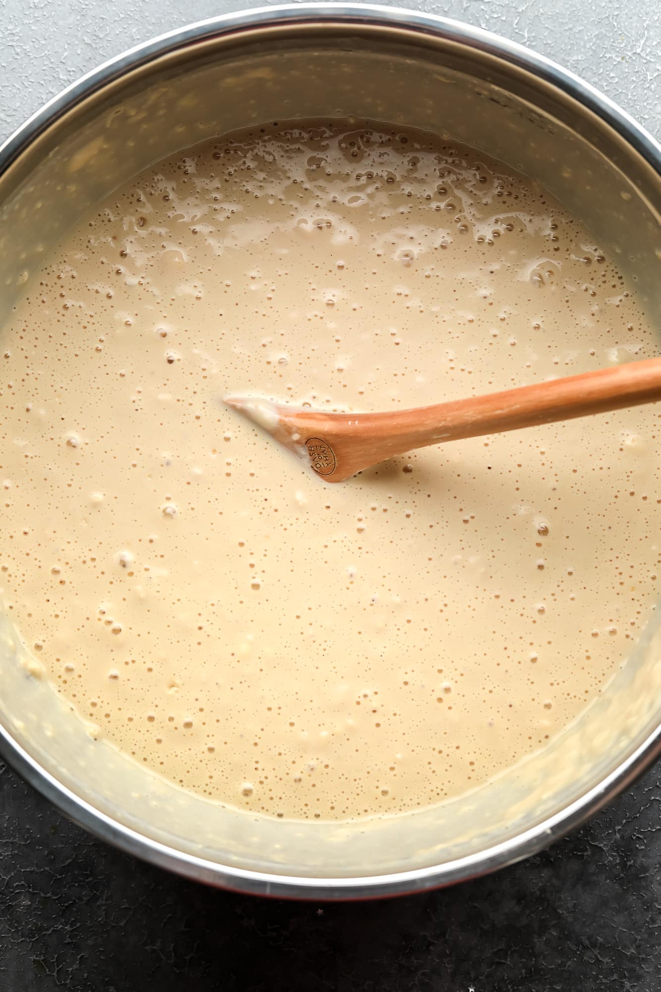 using a wooden spoon to stir vegan pancake batter in a large metal bowl.