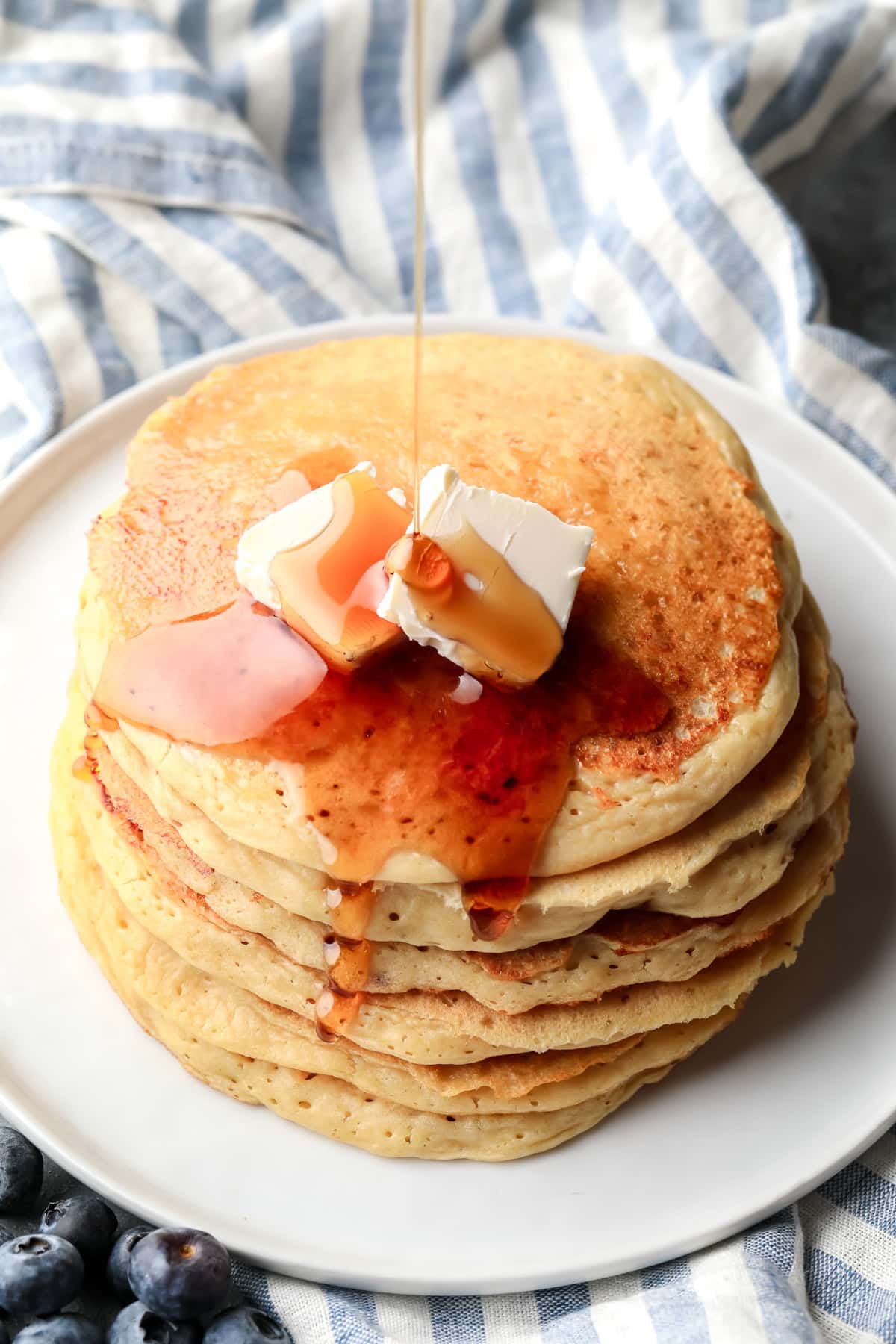 drizzling maple syrup on top of a stack of vegan protein pancakes.