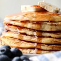 a stack of vegan protein pancakes topped with maple syrup and banana slices.