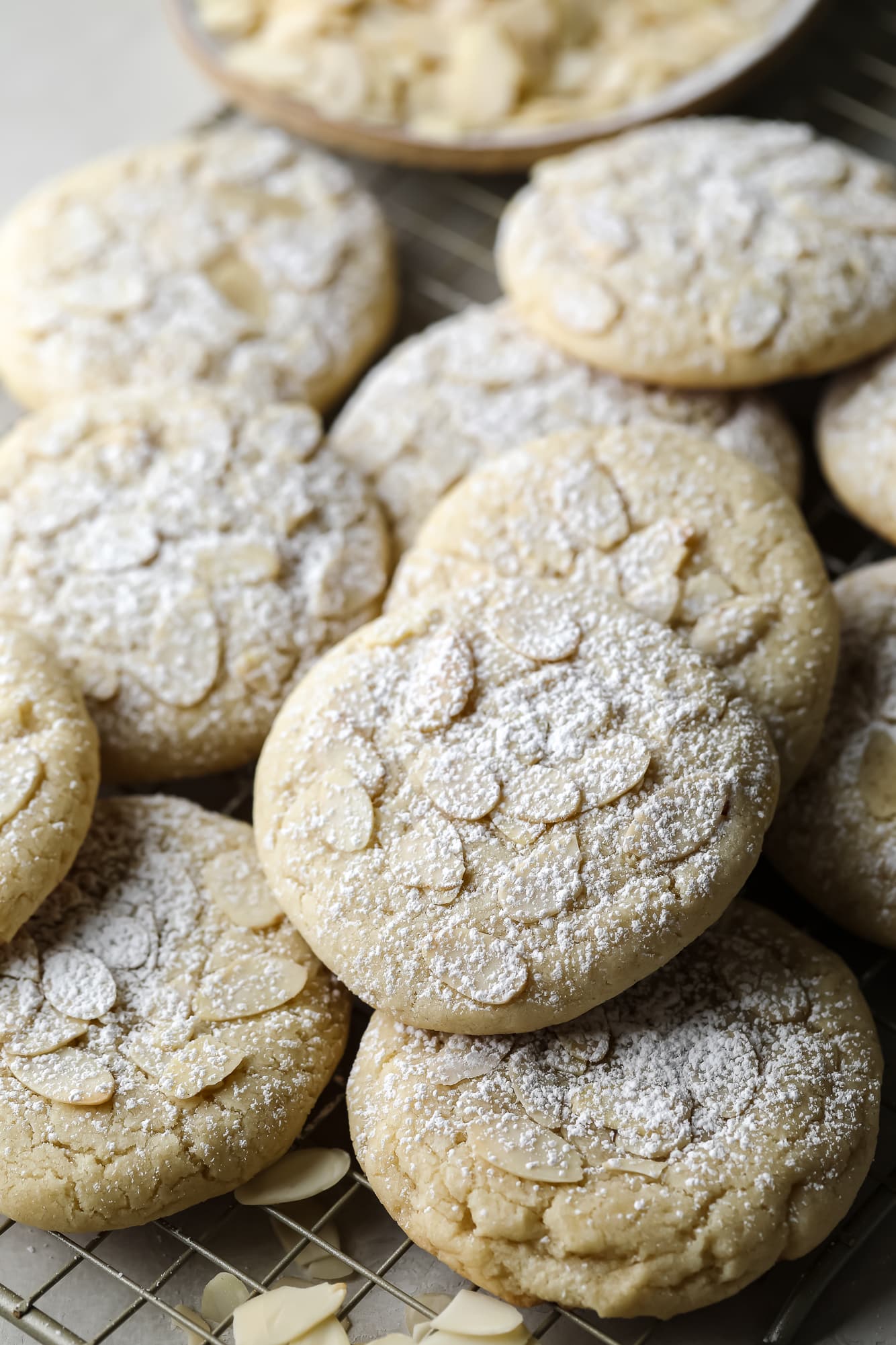 close up on a pile of Vegan Almond Croissant Cookies topped with sliced almonds and dusted with powdered sugar.