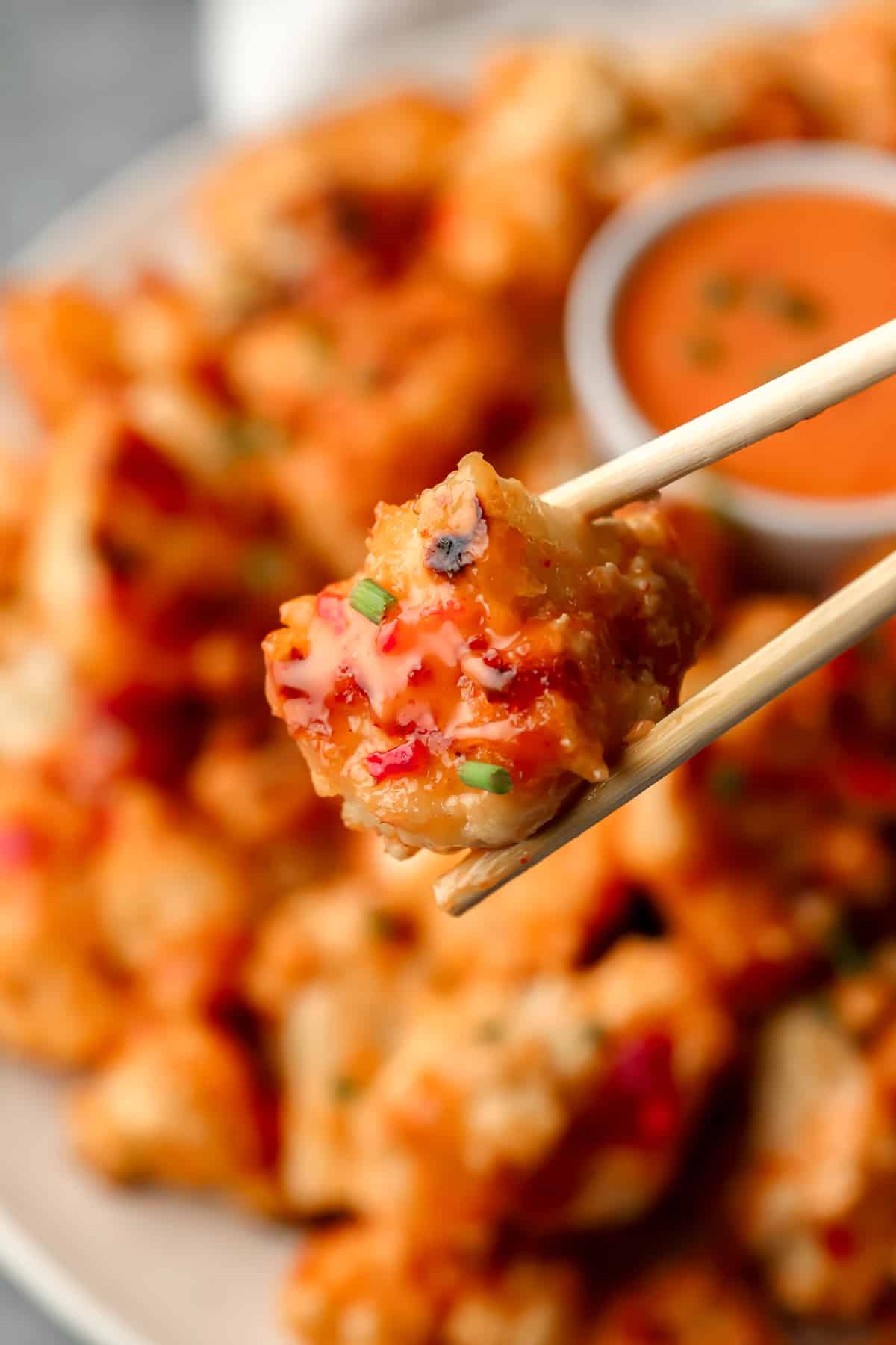 chopsticks holding up a cauliflower piece with more behind it on a plate