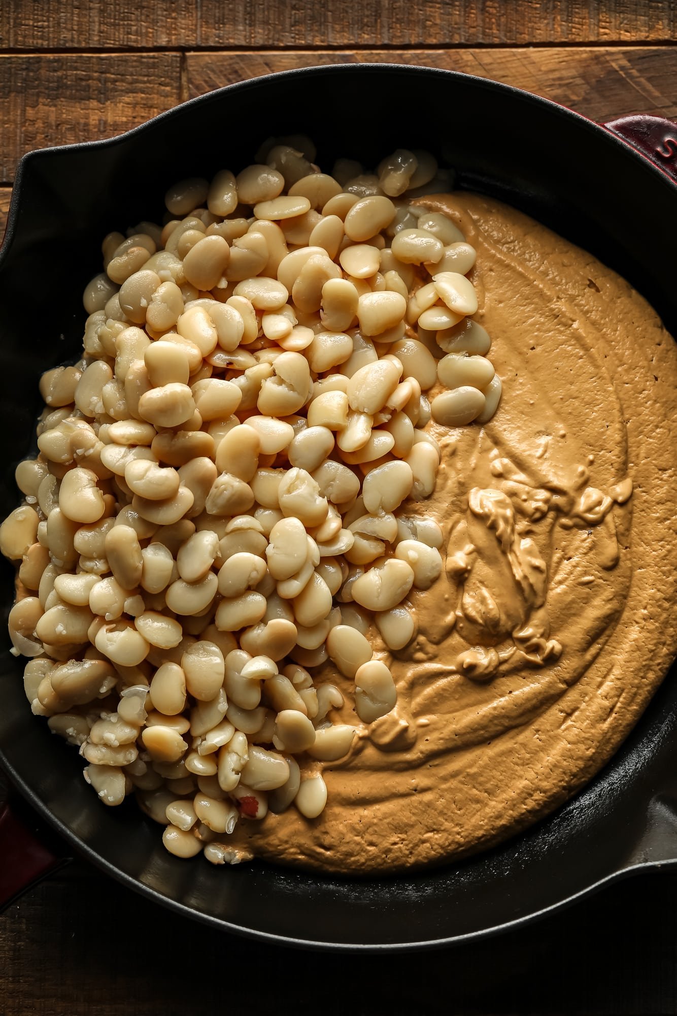 butter beans on top of a creamy Tuscan sun dried tomato sauce in a large black skillet.