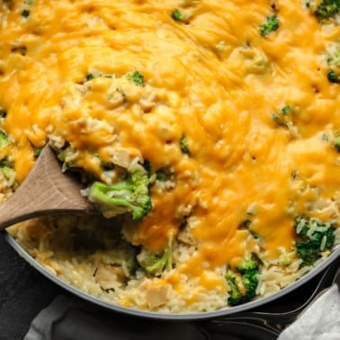 a wooden spoon in a cheese-covered broccoli and rice vegan casserole.