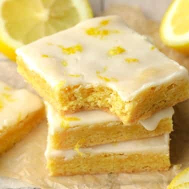 close up on a stack of yellow vegan lemon brownies topped with a lemon glaze.
