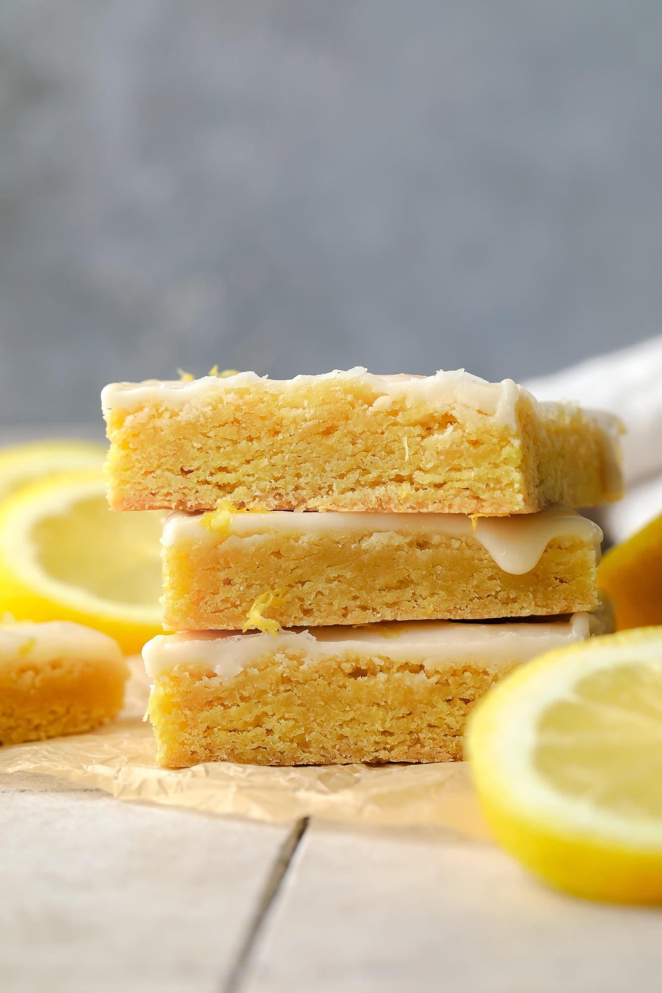 side view of a stack of yellow vegan lemon brownies topped with a lemon glaze.