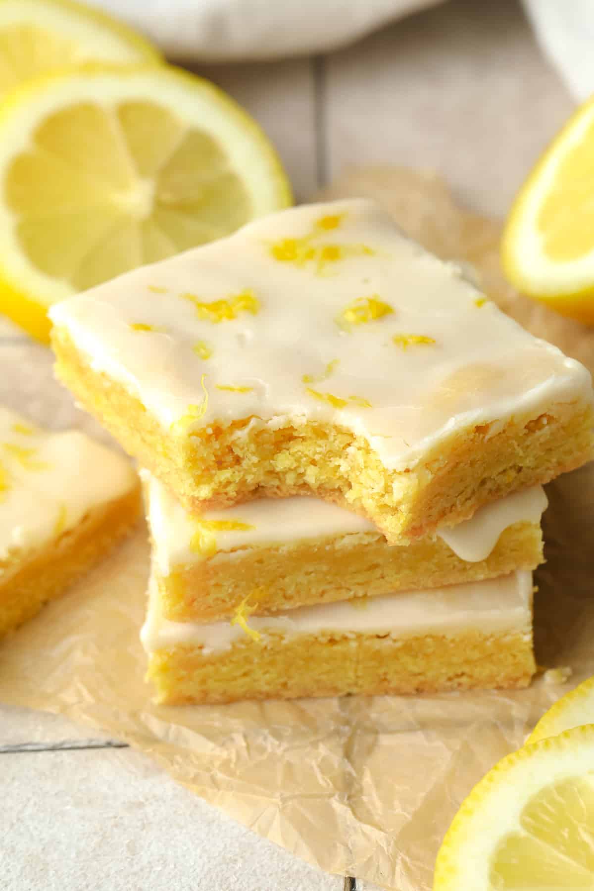 a stack of yellow vegan lemon brownies topped with a lemon glaze.