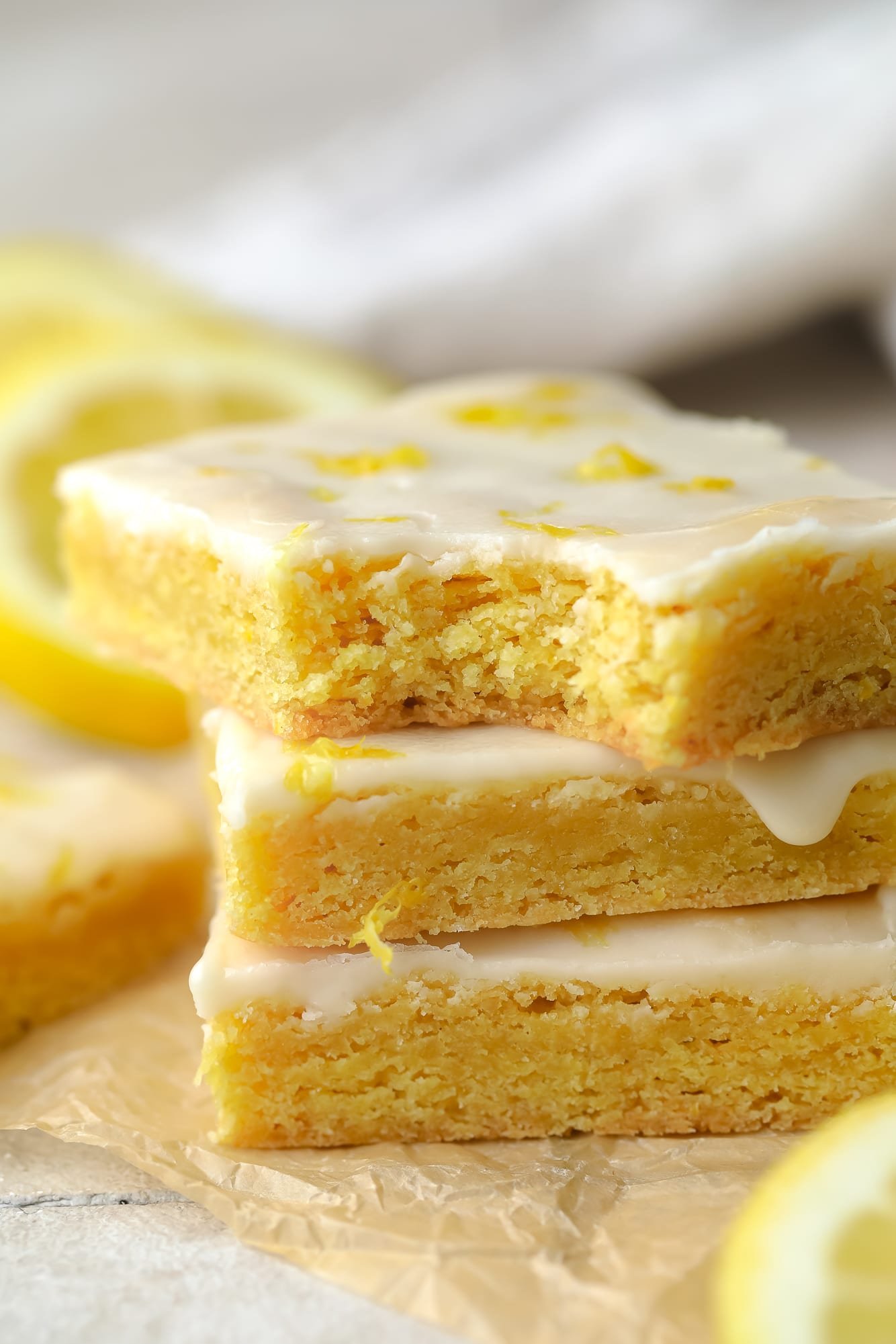 a stack of yellow vegan lemon brownies topped with a lemon glaze.