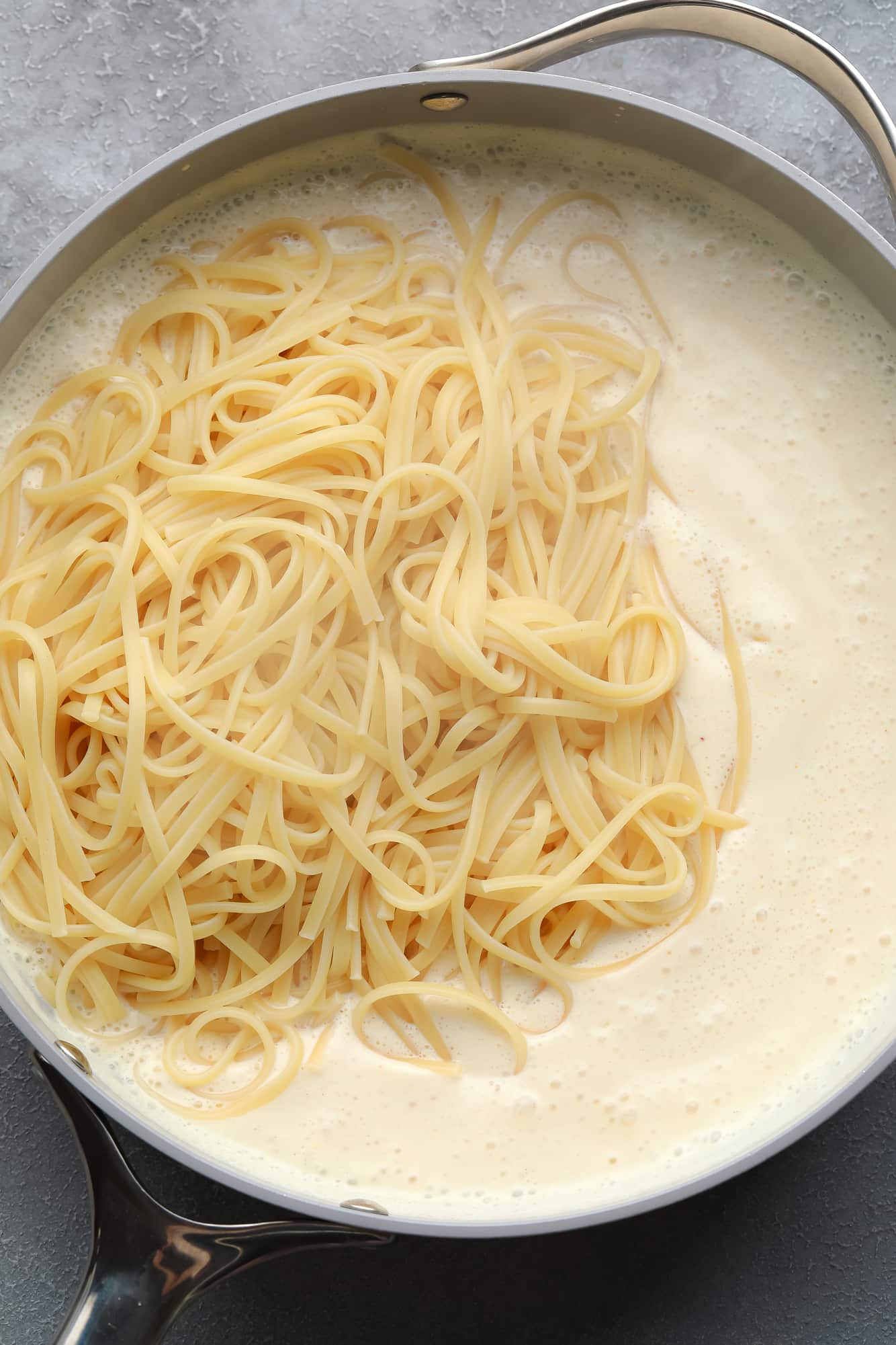 cooked pasta on top of a white, creamy sauce in a large pot.