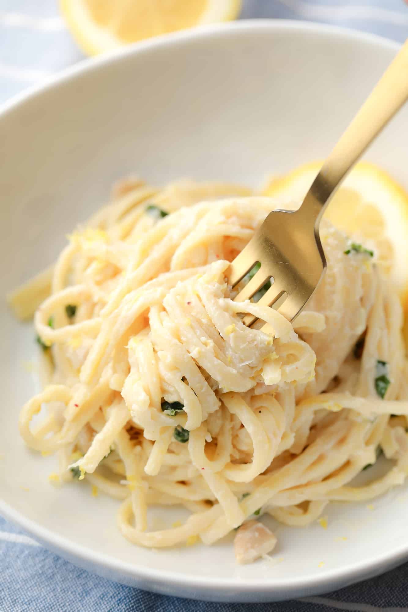 a fork scooping up lemon pasta from a white bowl.