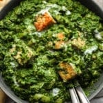 close up on golden tofu cubes tossed in a batch of vegan palak paneer in a black bowl.