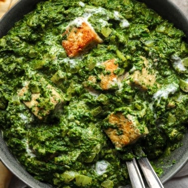 close up on golden tofu cubes tossed in a batch of vegan palak paneer in a black bowl.