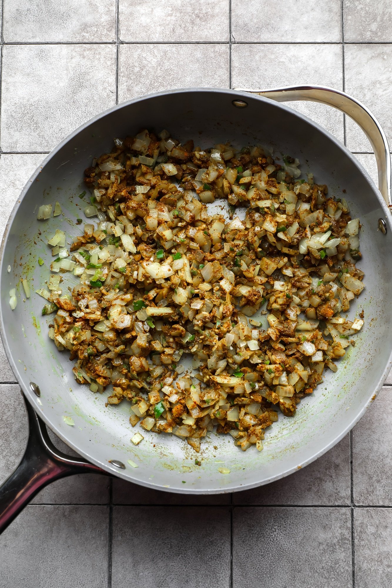 a seasoned mix of sauteed aromatics in a large metal skillet.