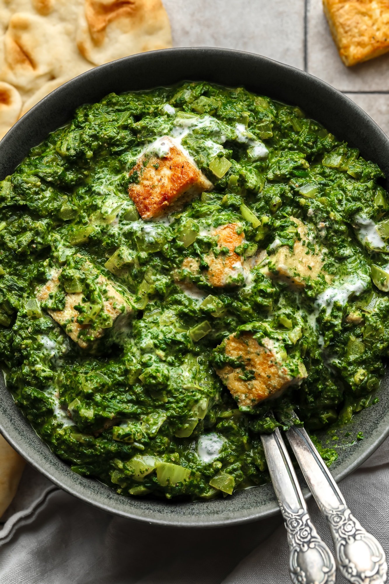 close up on golden tofu cubes tossed in a batch of vegan palak paneer in a black bowl.