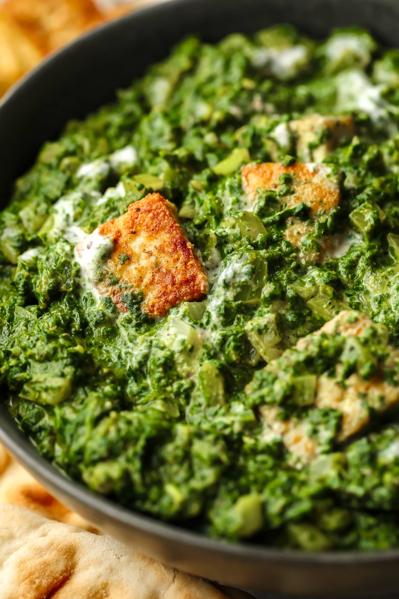 close up on golden tofu cubes tossed in a batch of vegan palak paneer in a black bowl.