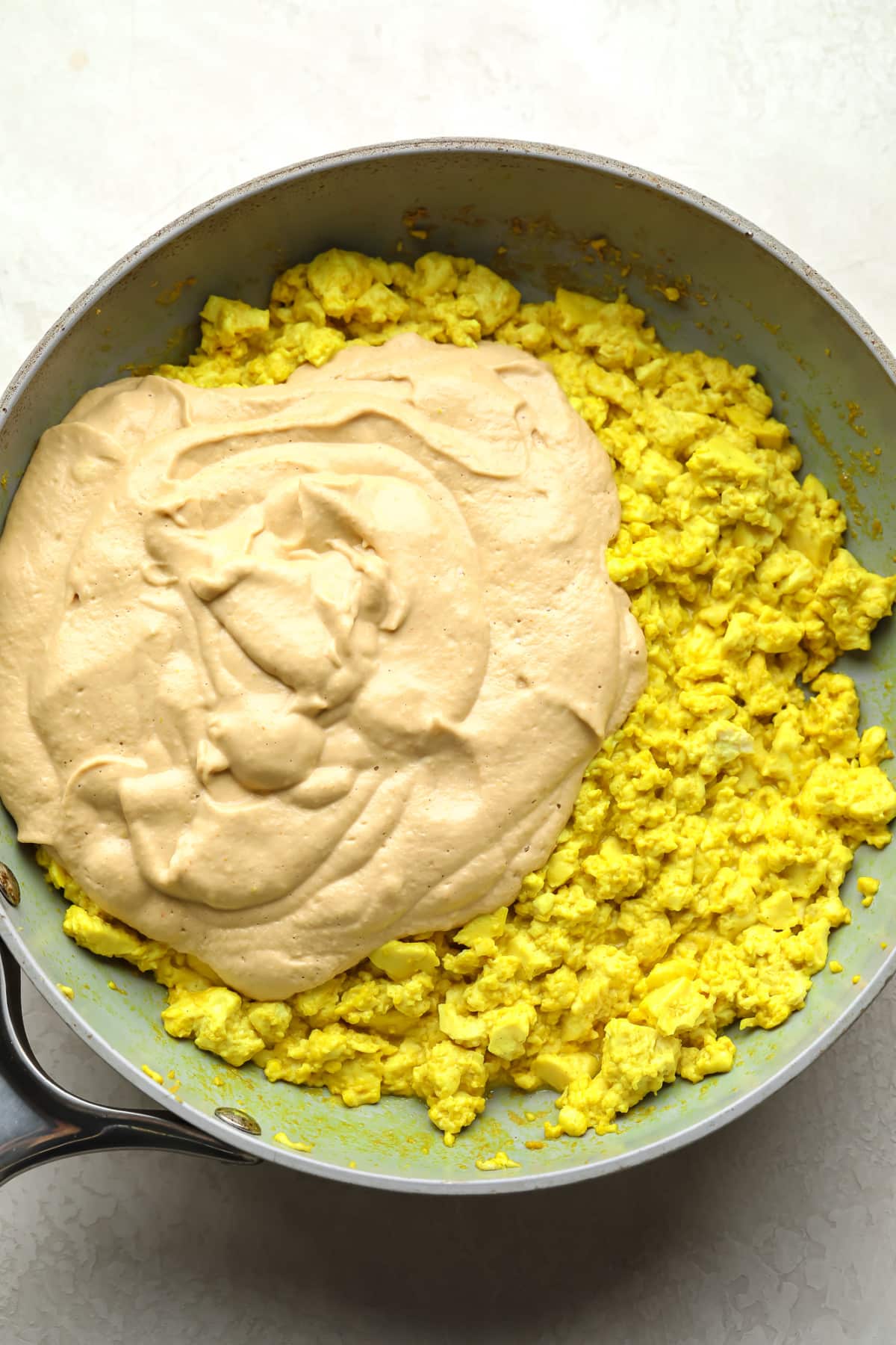 tofu scramble yellow with creamy sauce being added to a pan