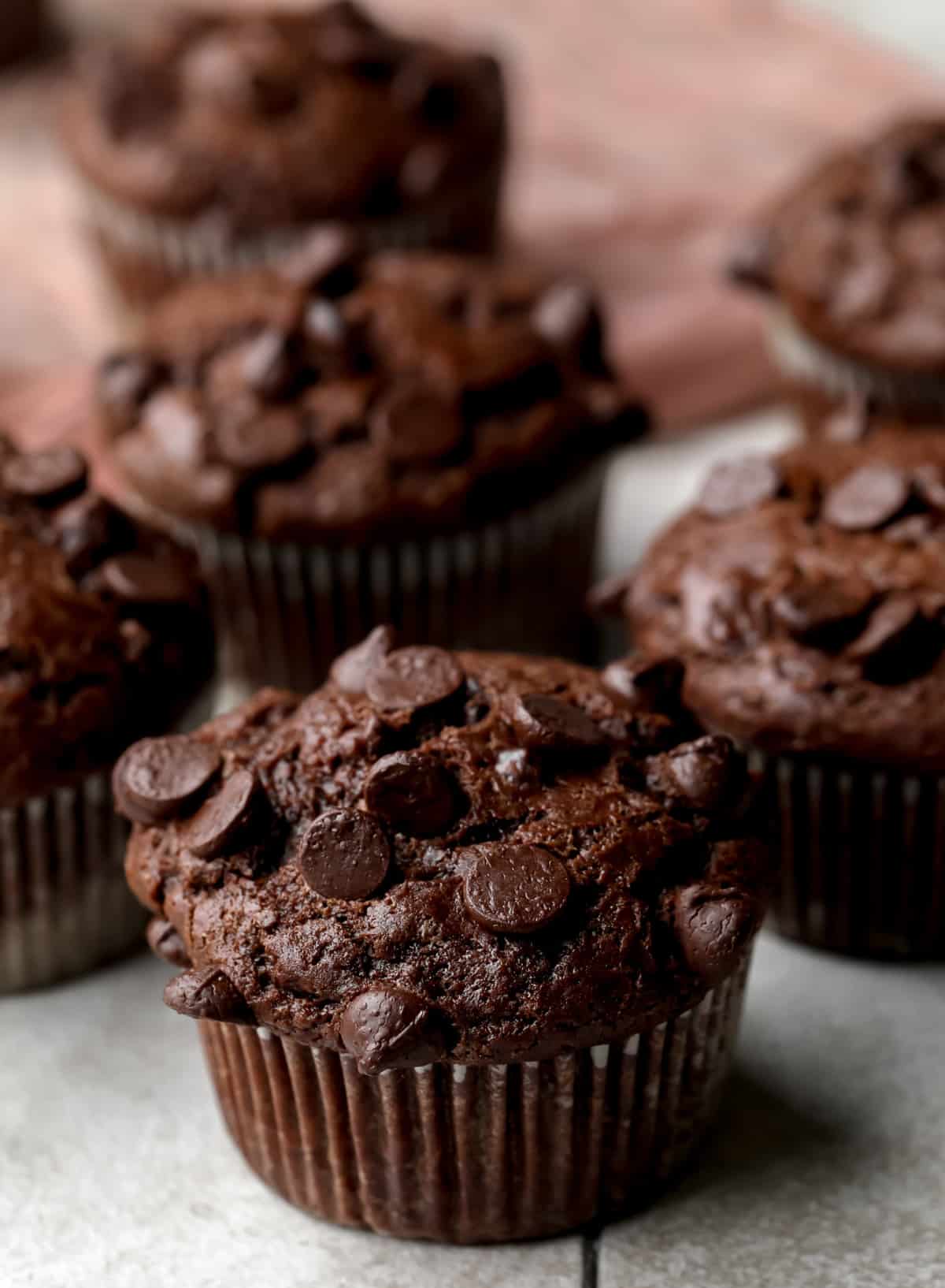 lots of vegan chocolate muffins on grey backdrop with pink towel