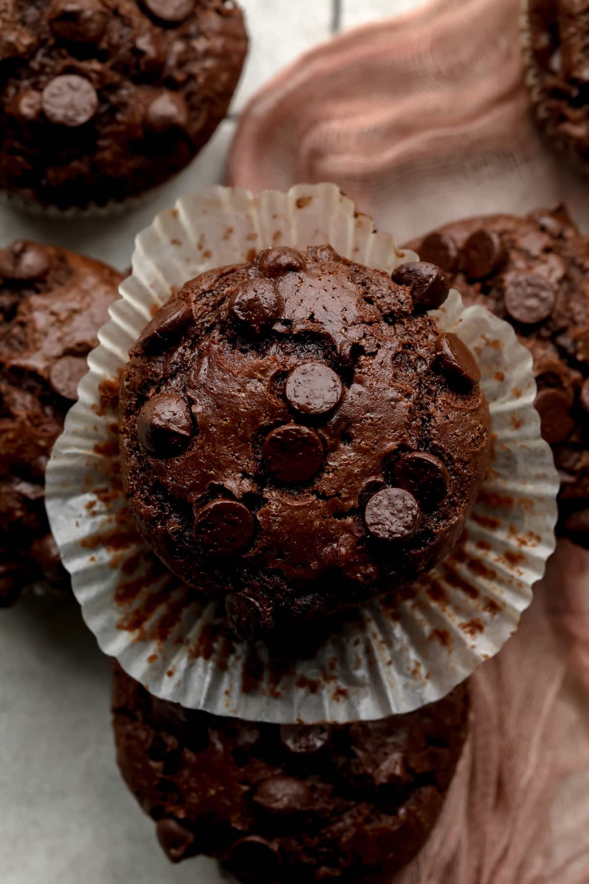 looking down on a double chocolate muffin, paper liner open around it and pink towel in background