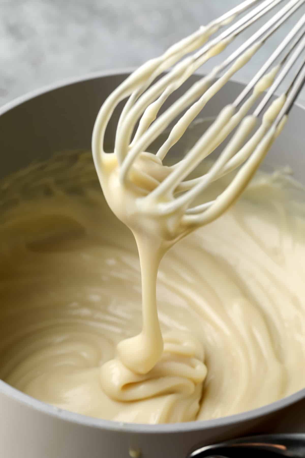 close up on a whisk drizzling vegan custard into a pot with more custard.
