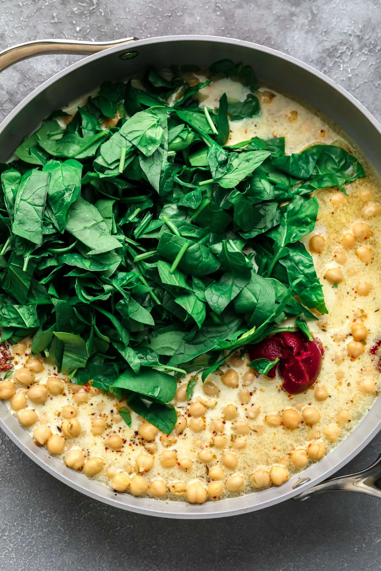 fresh spinach in a large pan with chickpeas and cream sauce.