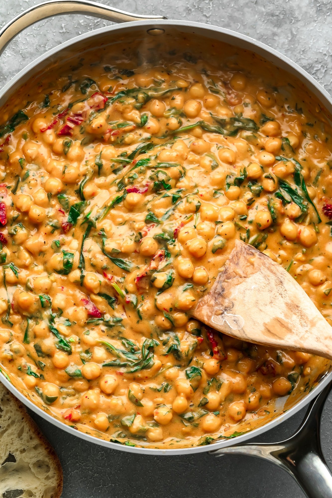 a wooden spoon stirring a batch of Marry Me Chickpeas in a large skillet.