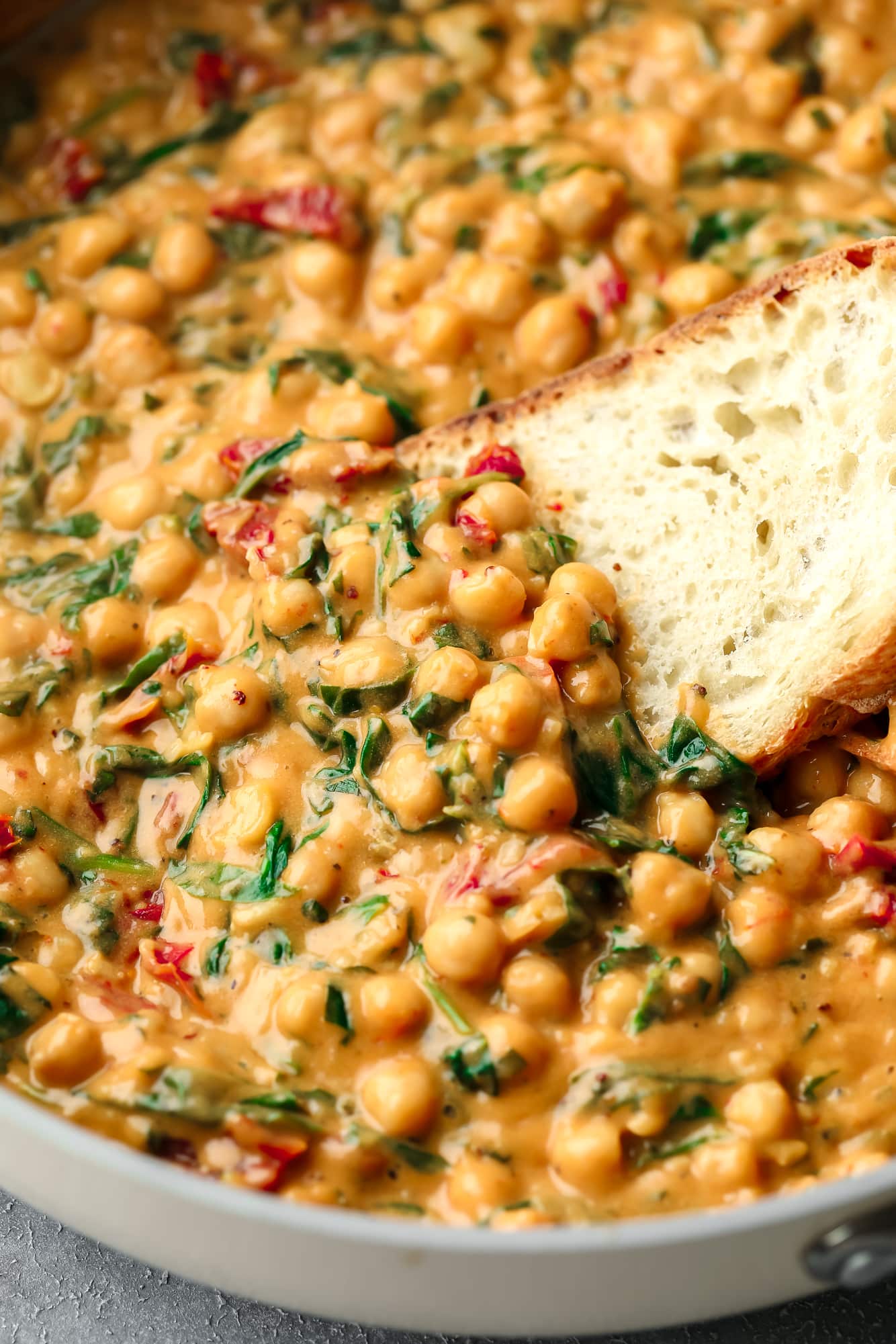 using a piece of bread to scoop up a bite of Marry Me Chickpeas from a skillet.