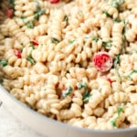 close up on creamy tahini pasta in a large skillet with tomatoes and basil.