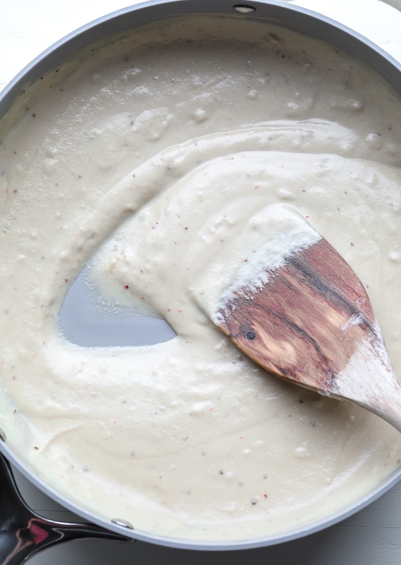 stirring a creamy tahini sauce in a saucepan with a wooden spoon.