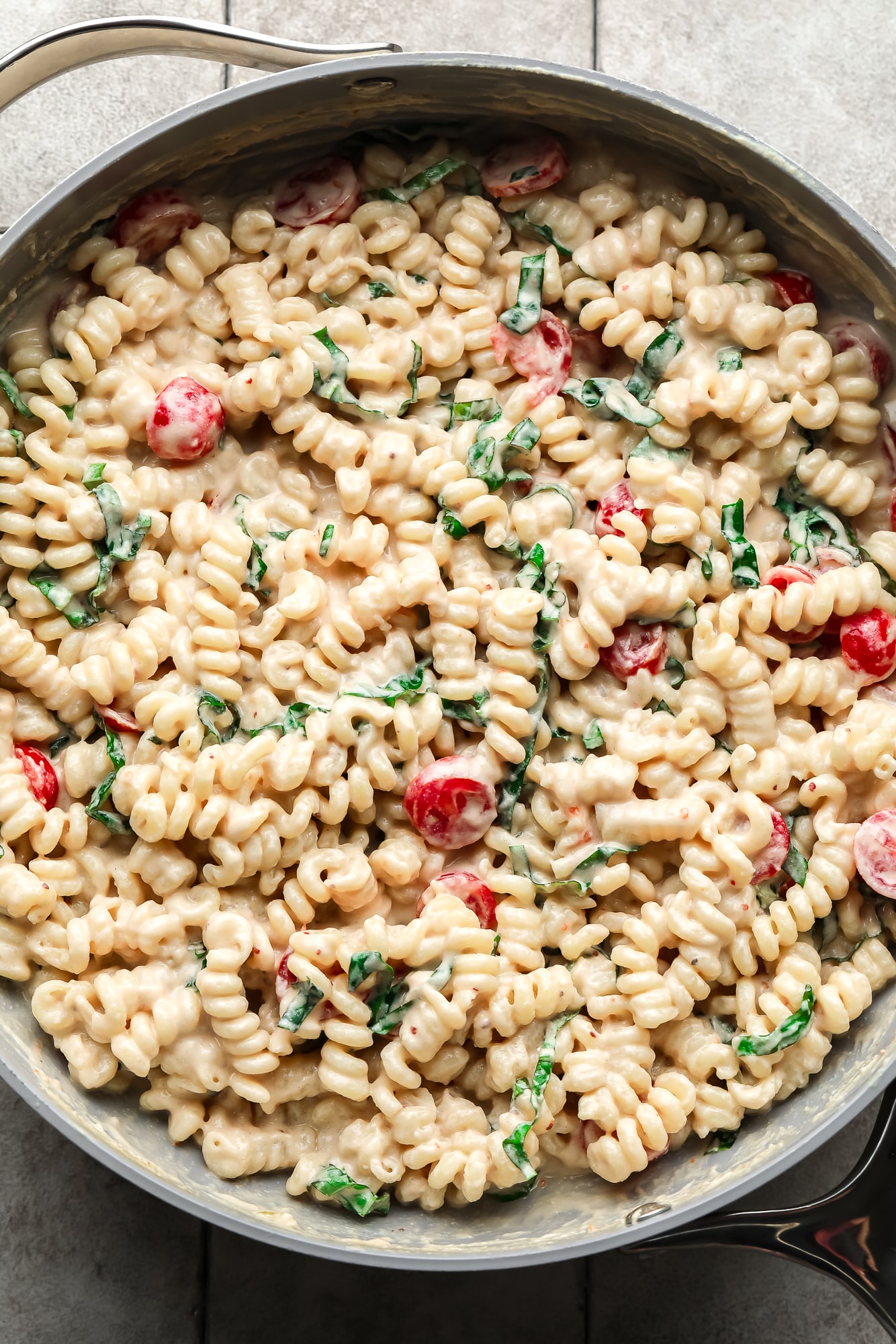 creamy tahini pasta in a large skillet with tomatoes and basil.