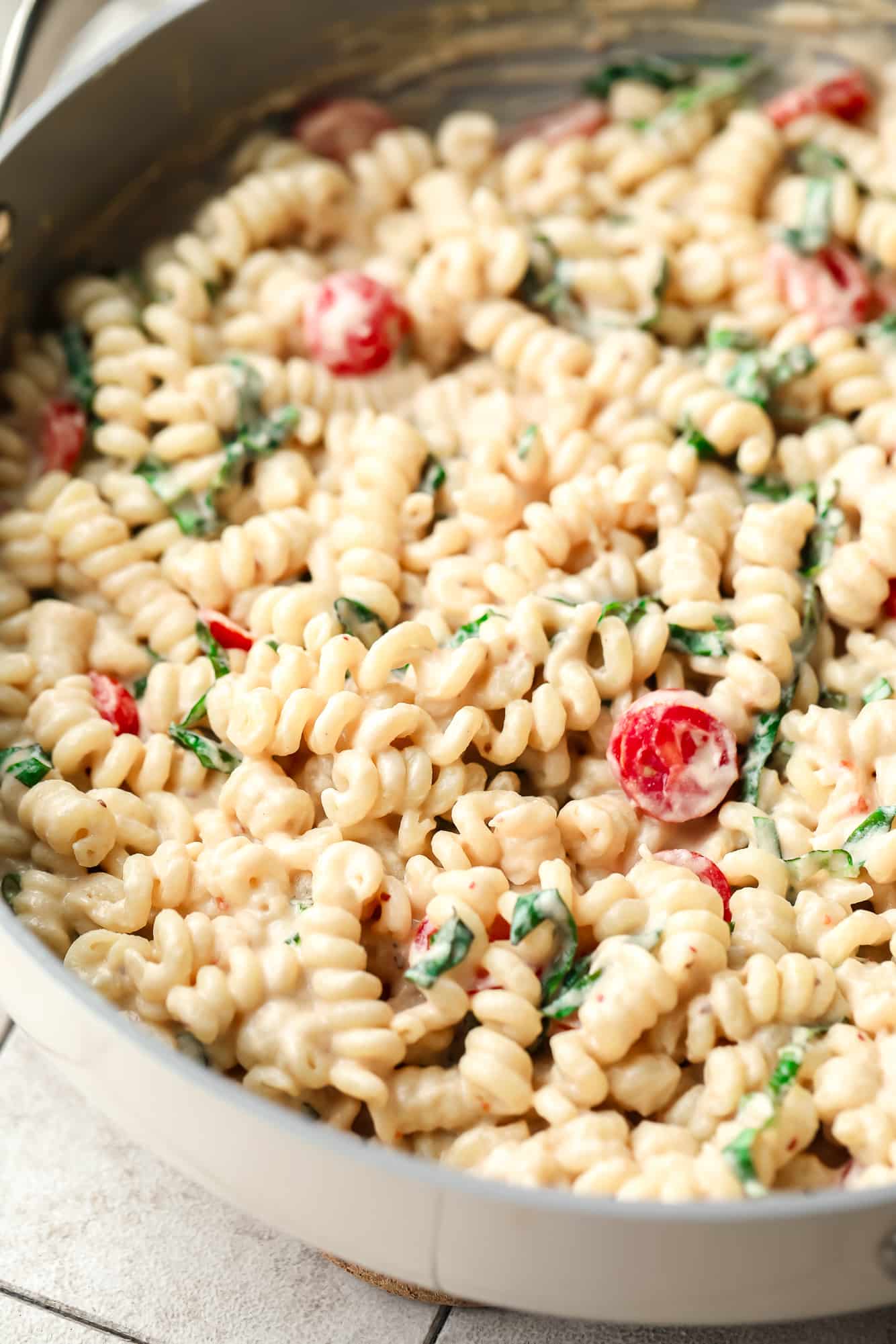 close up on creamy tahini pasta in a large skillet with tomatoes and basil.