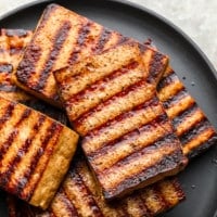 a pile of grilled tofu pieces on a black plate.