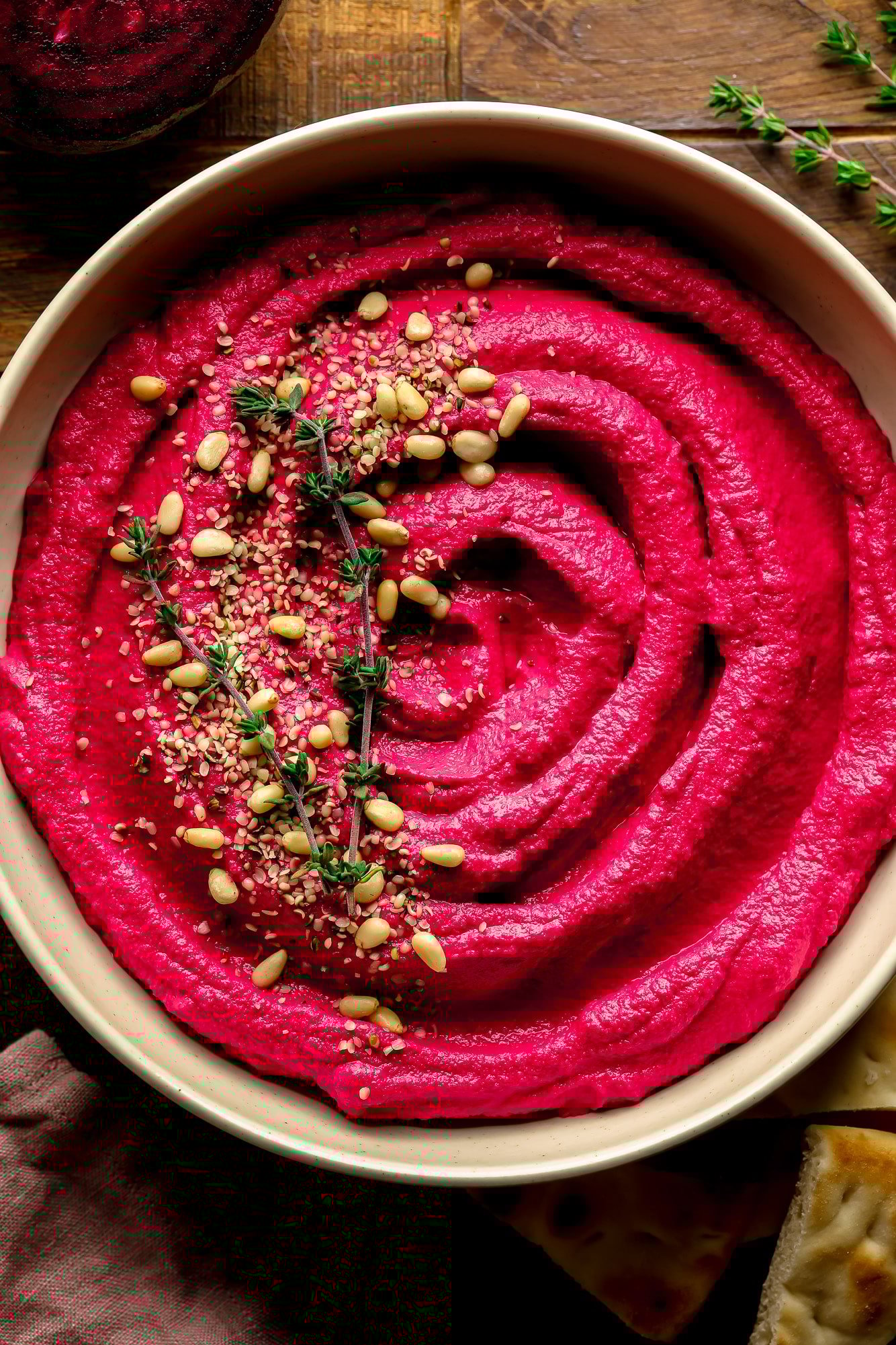 a bowl of pink beet hummus with pine nuts and thyme on top.