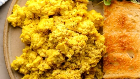 close up on a pile of yellow tofu scramble on a plate with toast, greens, and berries.