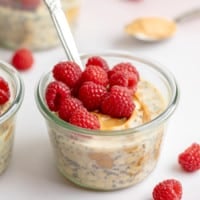 close up on a jar of peanut butter overnight oats topped with fresh raspberries.