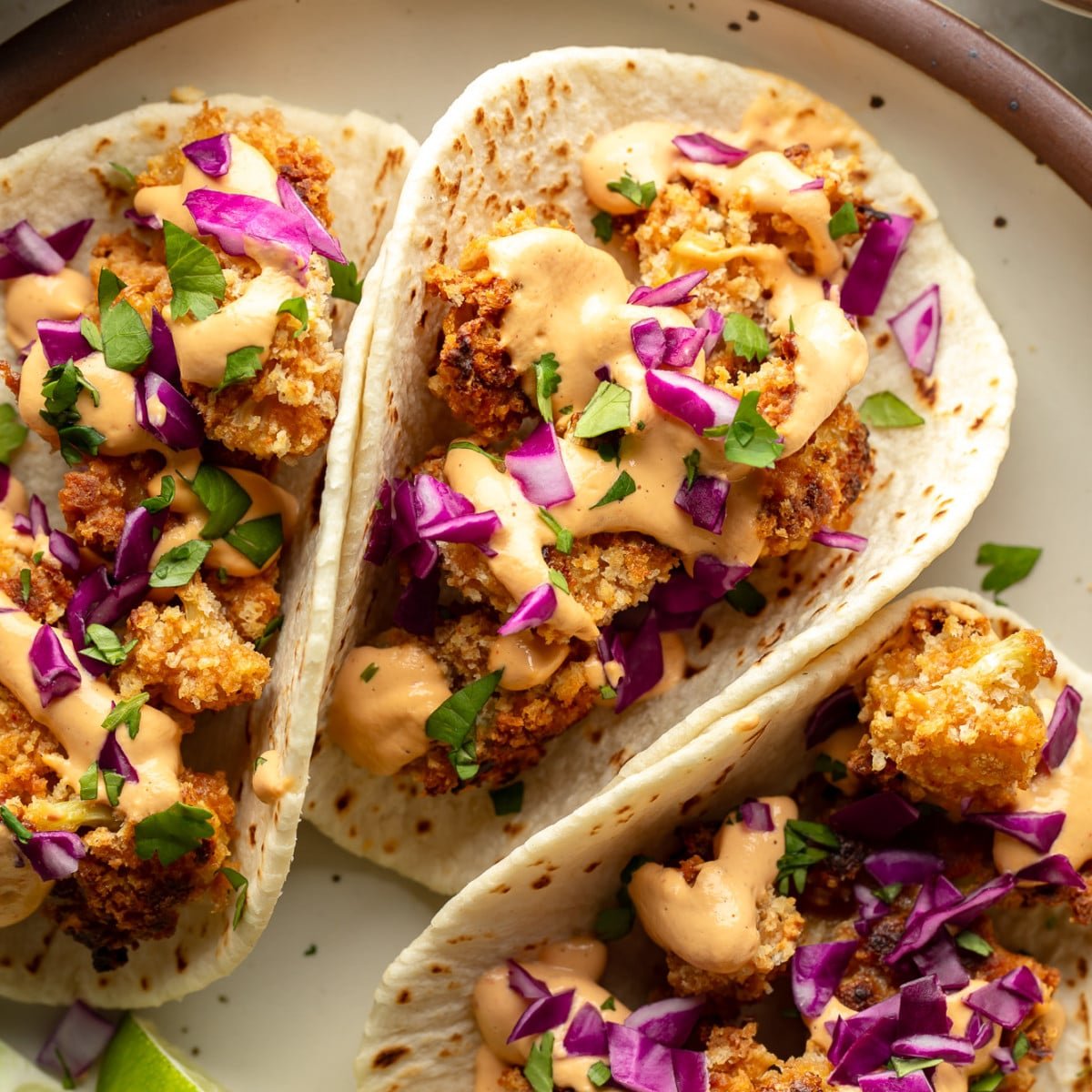 close up on 3 crispy cauliflower tacos on a plate.