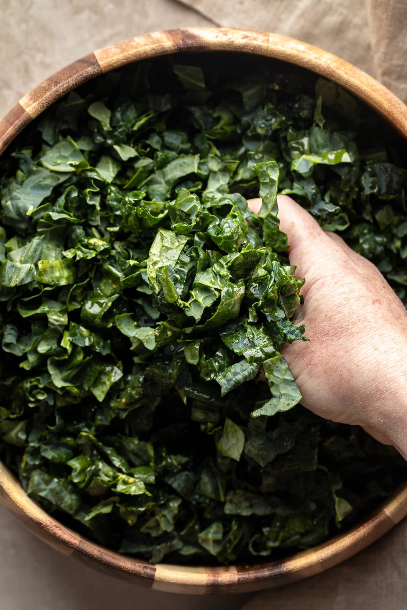womans hands massaging kale leaves in a large salad bowl.
