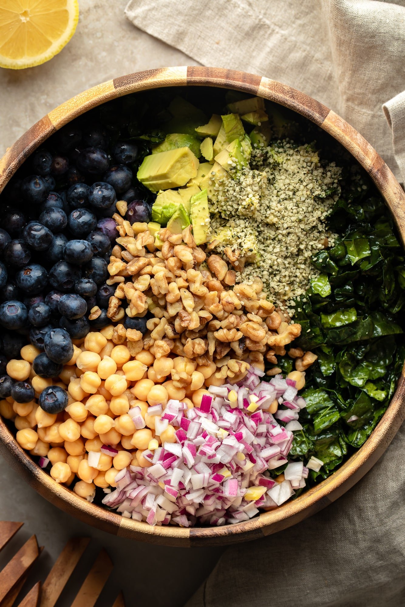 a kale salad topped with seeds, nuts, beans, veggies, and fruits in a large salad bowl.