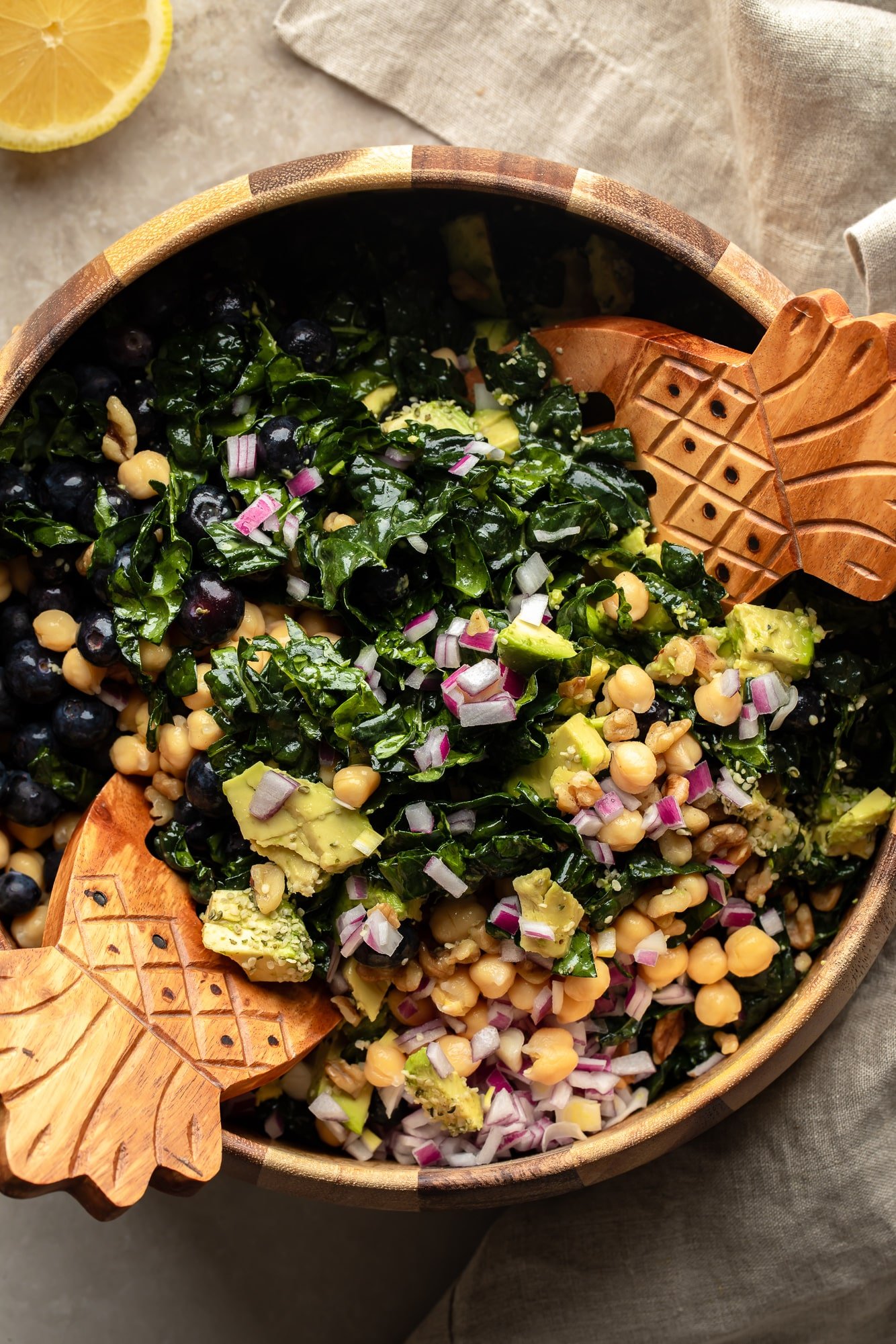 using 2 tongs to toss a kale salad together in a large bowl.