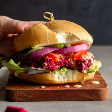 a woman's hand on a kidney beet burger with a bite taken out of it.
