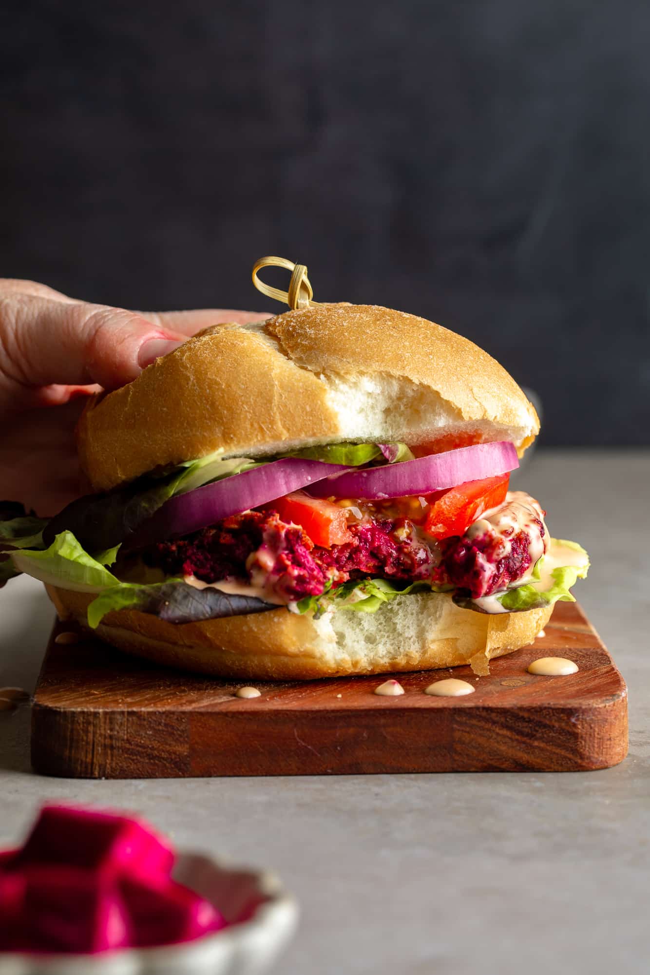 a woman's hand on a kidney beet burger with a bite taken out of it.