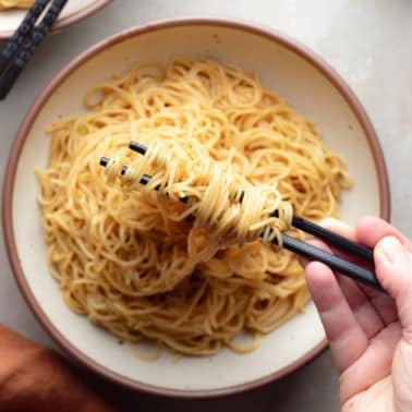 a hand using chopsticks to lift garlic noodles up from a bowl.