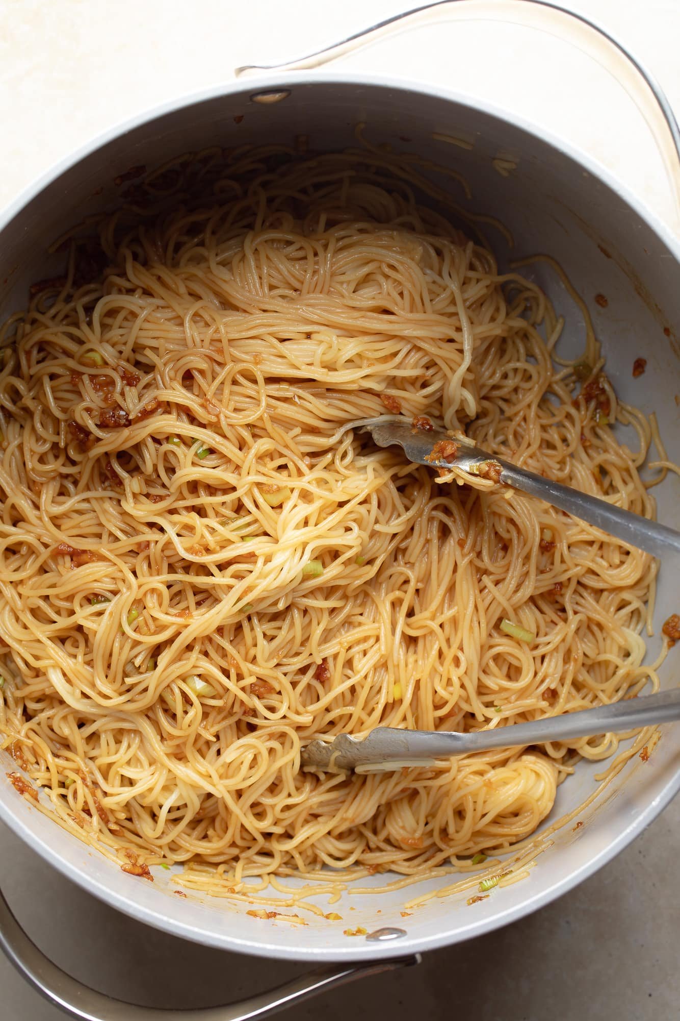 using tongs to toss cooked noodles in garlic sauce.