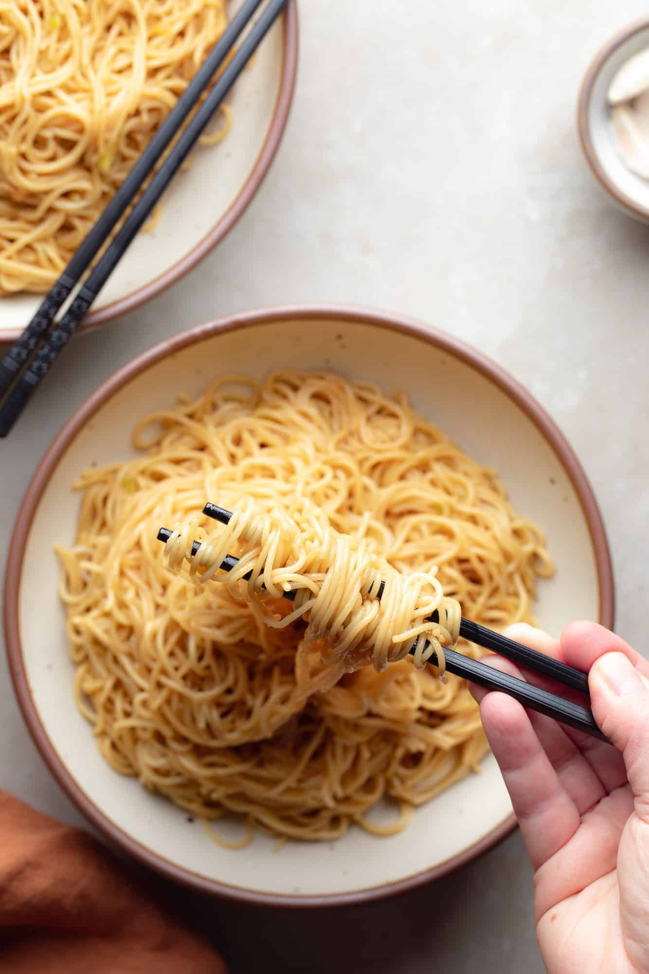 a hand using chopsticks to lift garlic noodles up from a bowl.