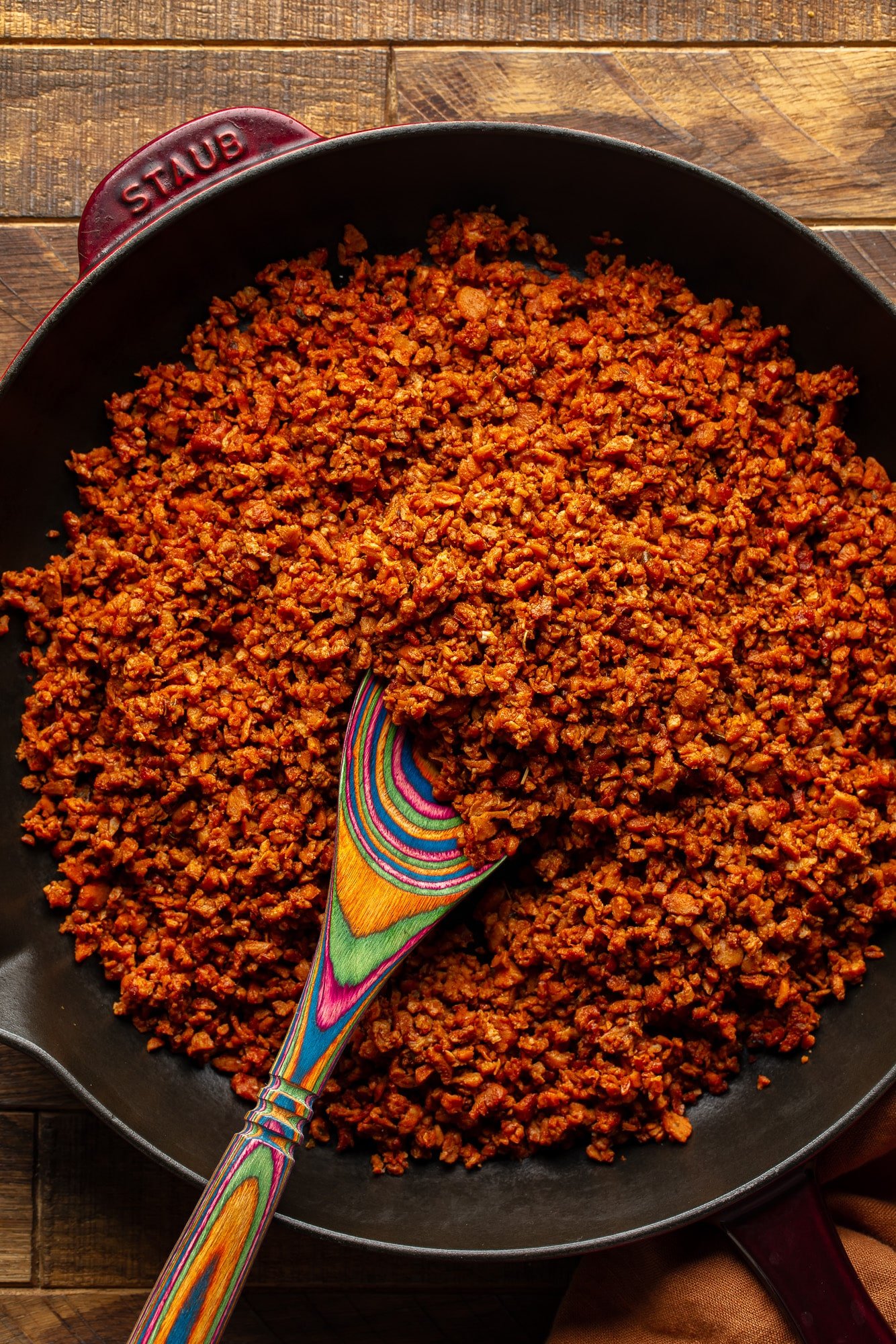 using a wooden spoon to stir vegan chorizo in a large skillet.