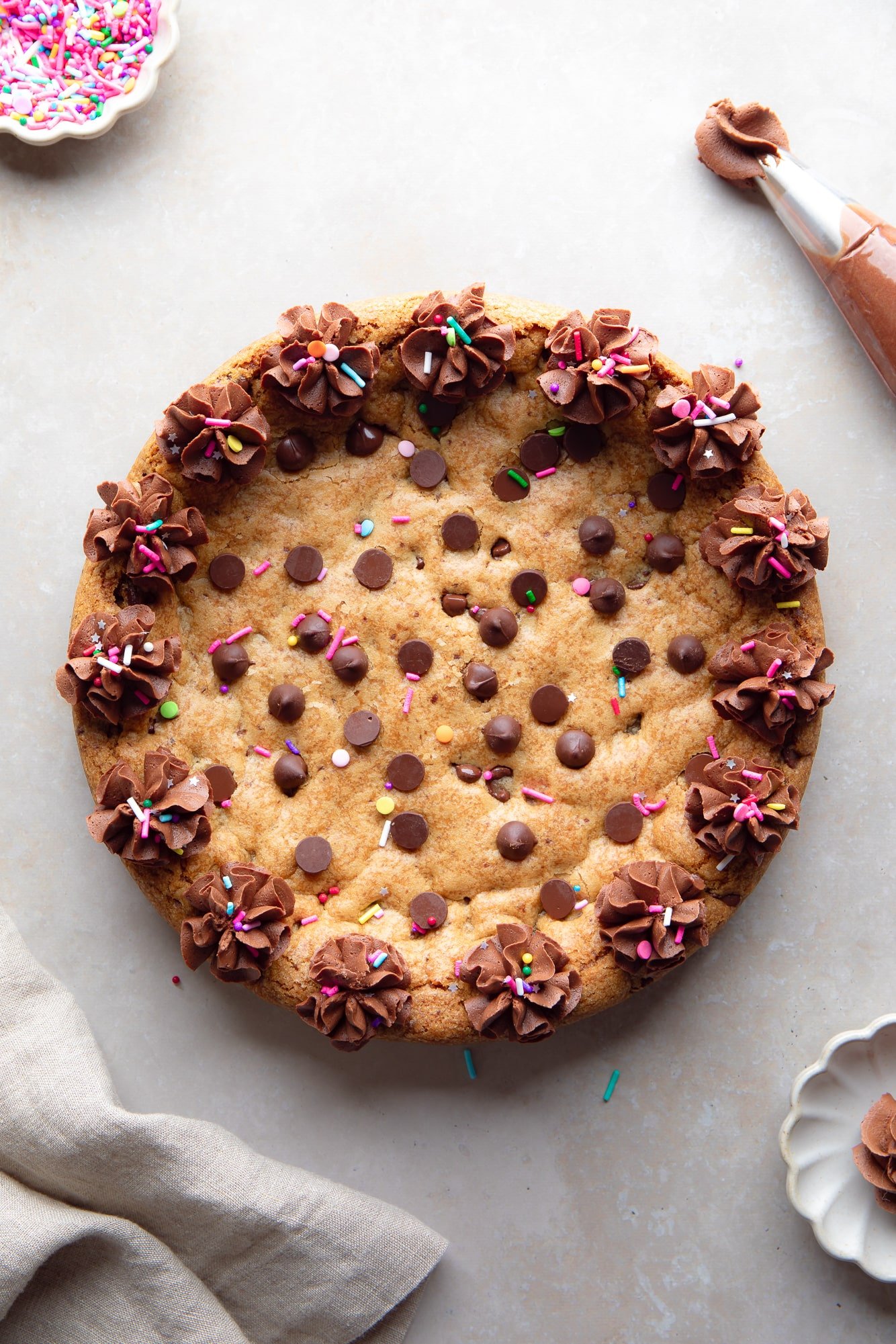 overhead view of a vegan cookie cake decorated with piped chocolate frosting and sprinkles.