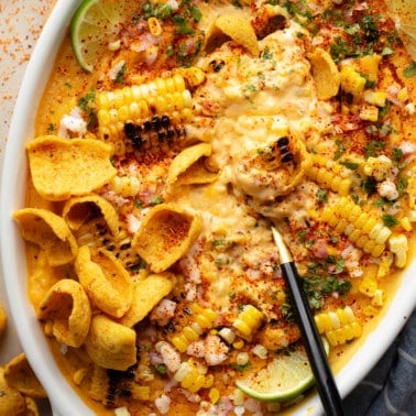 close up on a black spoon in a batch of vegan Mexican street corn dip in a baking dish.