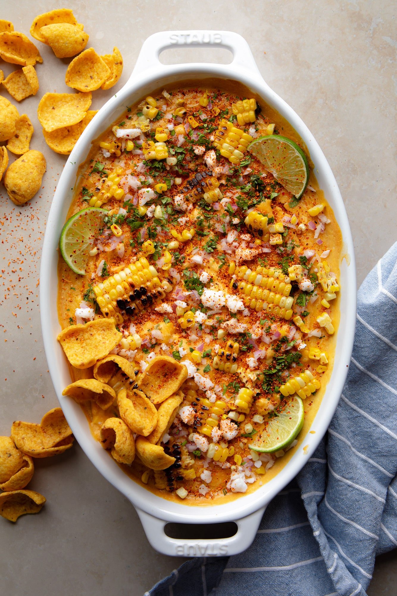 vegan Mexican street corn dip topped with charred corn, corn chips, and lime wedges in a baking dish.