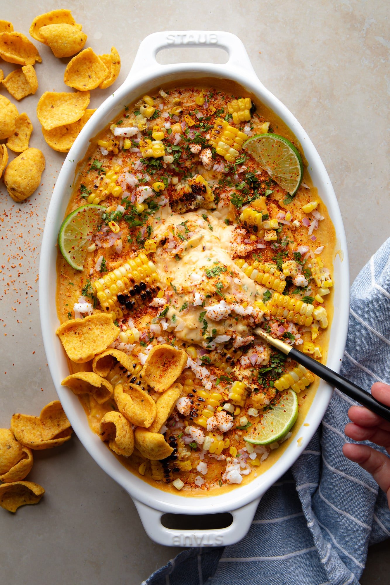 a black spoon in a batch of vegan Mexican street corn dip in a baking dish.