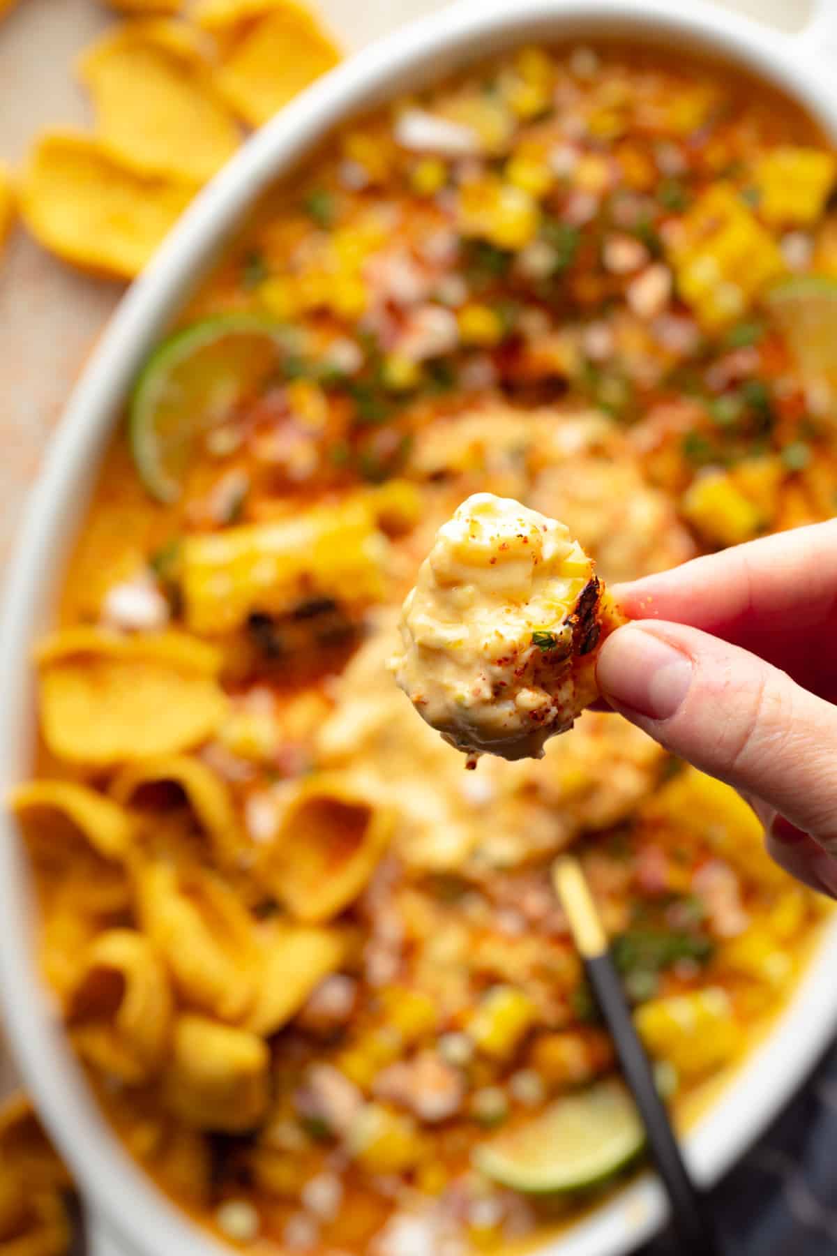 A woman's hand holding a corn chip with a scoop of vegan Mexican street corn dip.