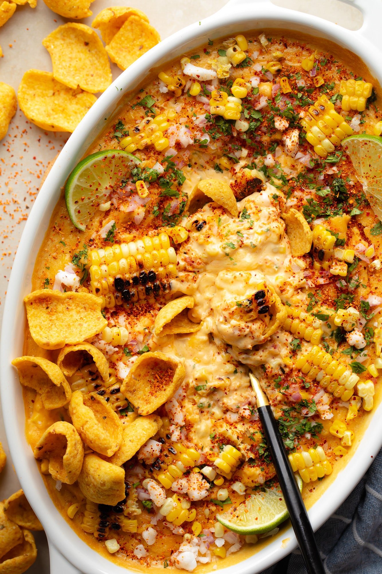 a black spoon in a batch of vegan Mexican street corn dip in a baking dish.